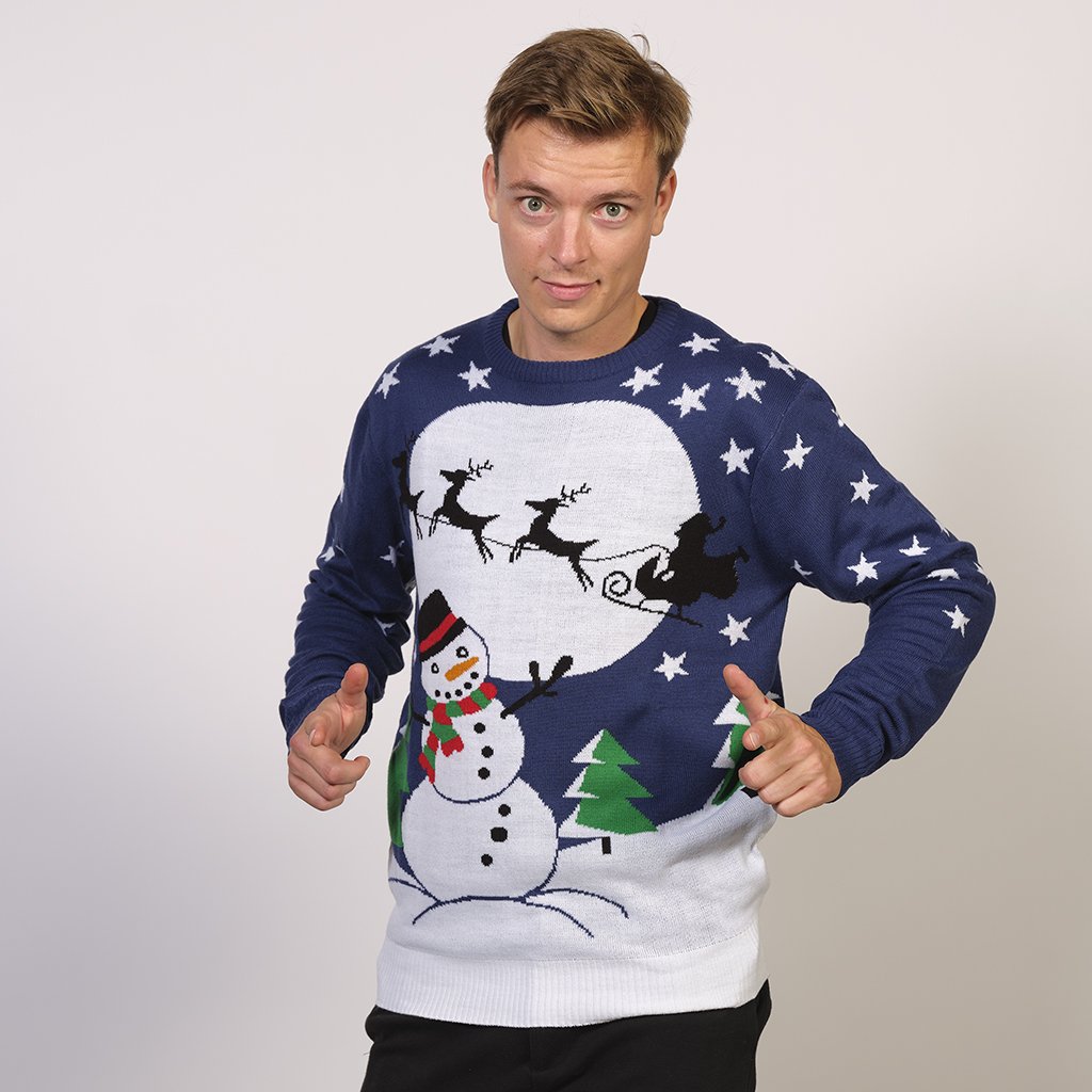 Un uomo in posa che indossa un maglione natalizio blu con un pupazzo di neve e una luna.